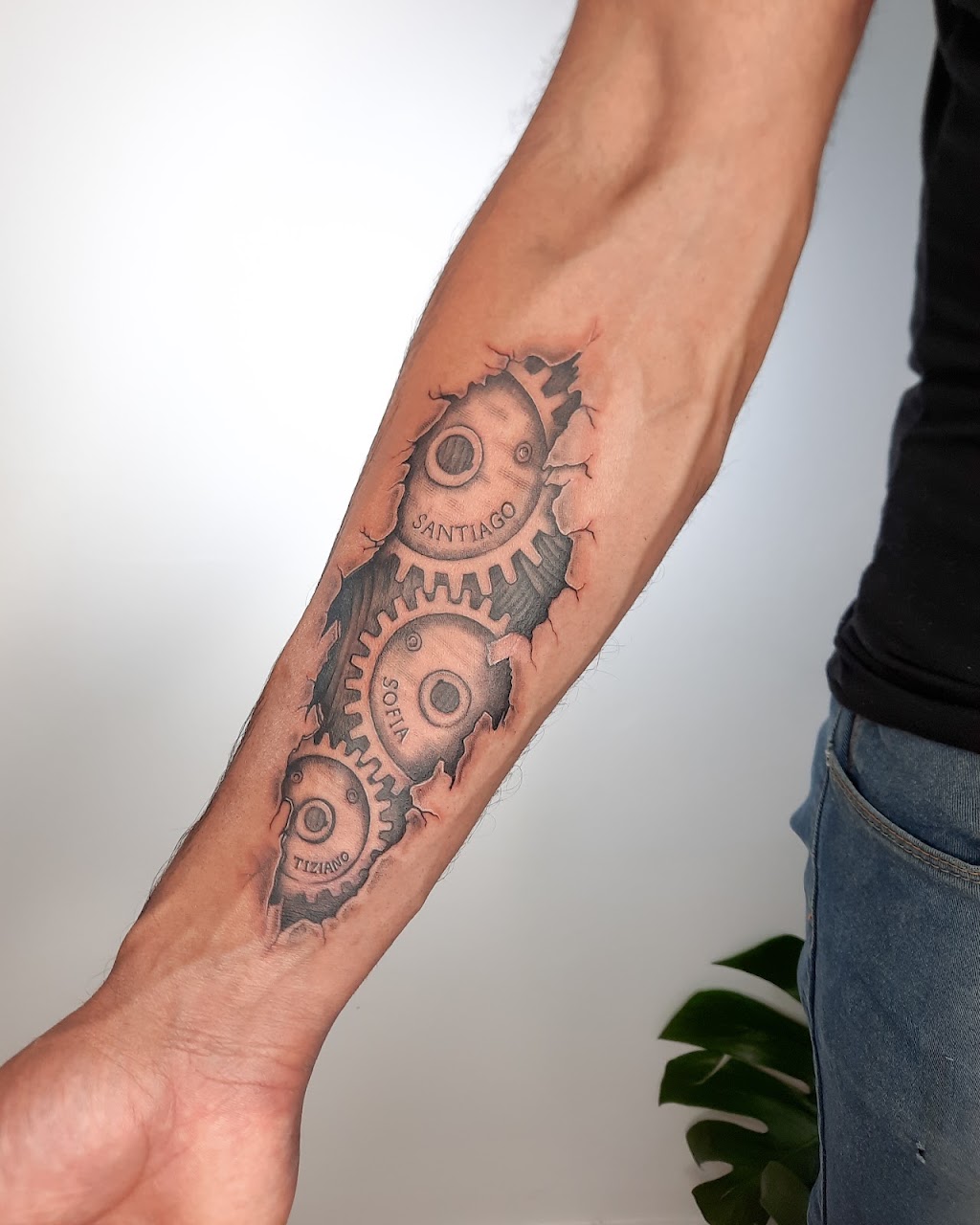 Antebrazo con tatuaje personalizado de engranajes, ejemplo de trabajo en negro